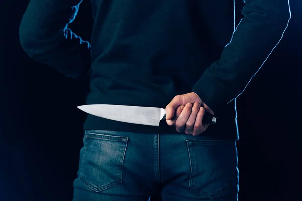 Cropped view of murderer hiding knife behind back on black — Stock Photo