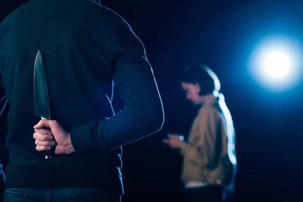 Cropped view of murderer hiding knife behind back on black — Stock Photo