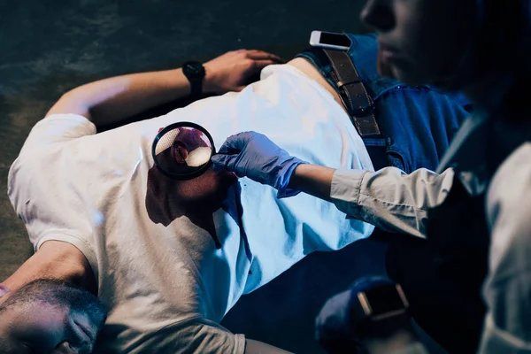 Partial view of investigator using magnifying glass at crime scene — Stock Photo