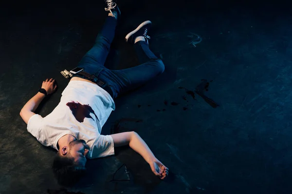 Overhead view of dead man with blood on t-shirt lying at crime scene — Stock Photo