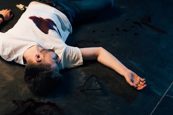 Dead man with blood on t-shirt on floor at crime scene — Stock Photo