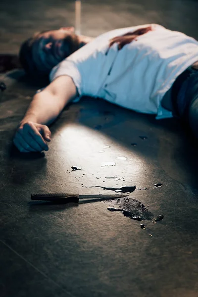Selective focus of dead man with blood on t-shirt on floor at crime scene — Stock Photo