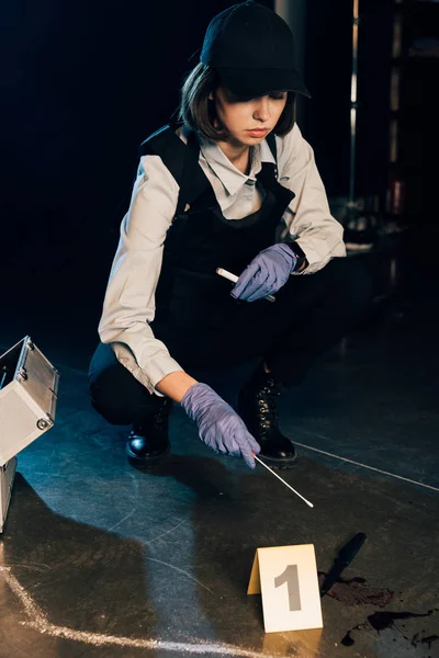 Investigaror in gloves holding test tube and swab at crime scene — Stock Photo