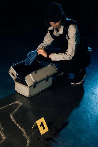 Investigator with investigation kit putting on rubber glove at crime scene — Stock Photo