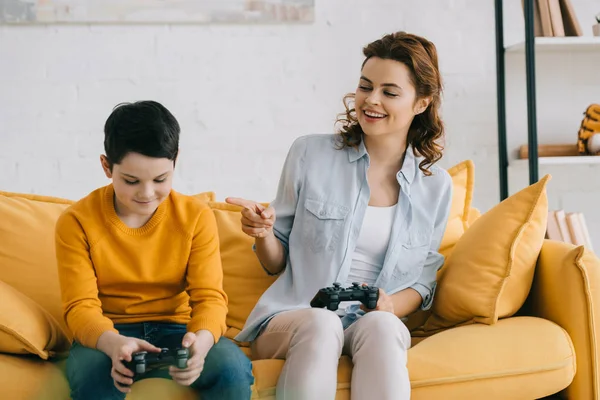 KYIV, UKRAINE - APRIL 8, 2019: Cheerful woman holding joystick and pointing with finger at upset son — Stock Photo