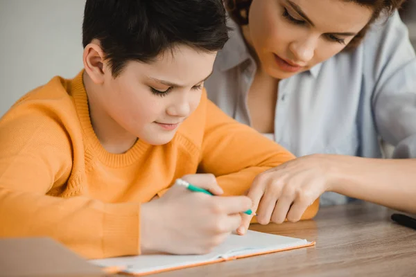 Schöne Frau hilft aufmerksamem Sohn bei Hausaufgaben — Stockfoto