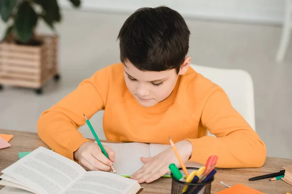 Aufmerksamer Junge liest Buch und schreibt in Kopierbuch, während er zu Hause Hausaufgaben macht — Stockfoto