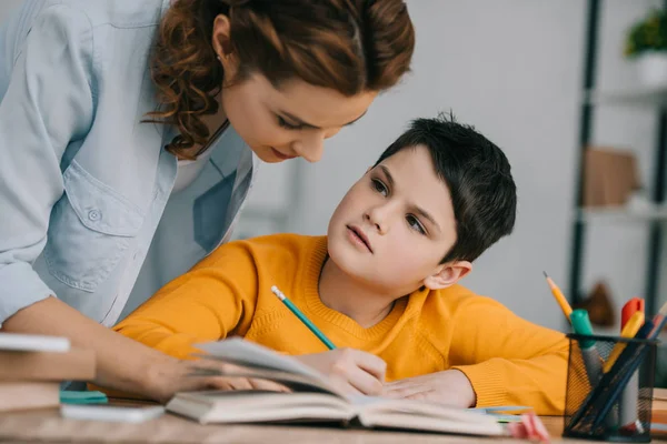 Hermosa mujer ayudando adorable hijo haciendo trabajo escolar en casa - foto de stock