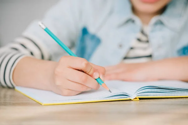 Partial view of schoolkid writing in copy book while doing homework — Stock Photo