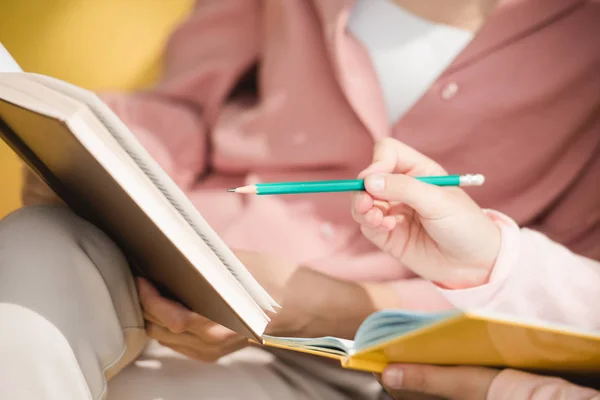 Частковий вигляд дитини, що вказує олівцем на книгу в руках матерів — стокове фото