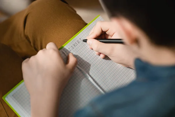 Foco selectivo de la escritura del colegial en libro de copia mientras que hace el trabajo escolar en el país - foto de stock