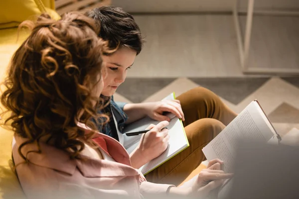 Selective focus of mother and son sitting on floor and making homework together — Stock Photo