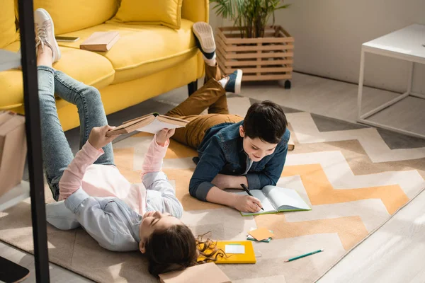 Чарівні діти лежать на підлозі вдома і роблять шкільну роботу разом — стокове фото