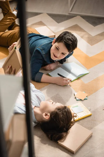 High angle view of cute brother and sister lying on floor and doing homework — Stock Photo