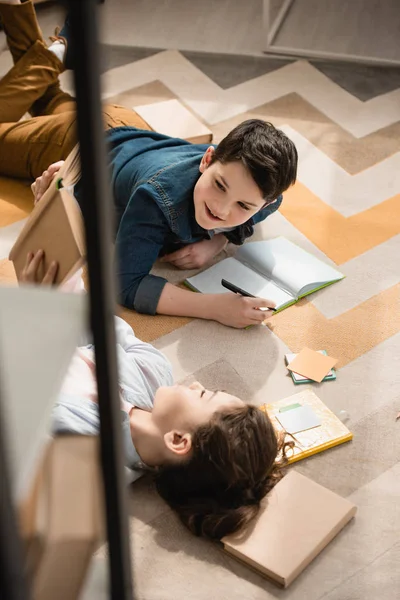 Vue grand angle de mignon frère et soeur couché sur le sol et faire des devoirs — Photo de stock