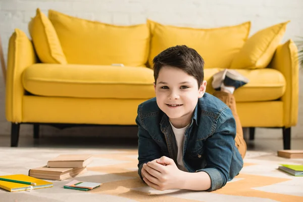 Lächelnder Junge blickt in die Kamera, während er auf dem Boden neben dem gelben Sofa liegt — Stockfoto