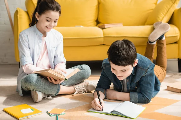 Adorable brother and sister doing schoolwork on floor at home together — Stock Photo