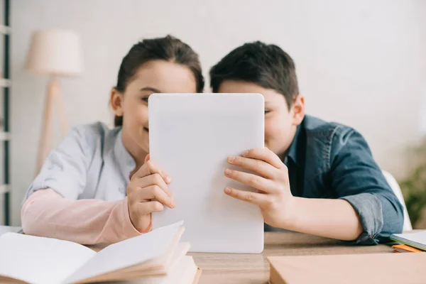 Brother and sister using digital together while sitting at desk with books — Stock Photo