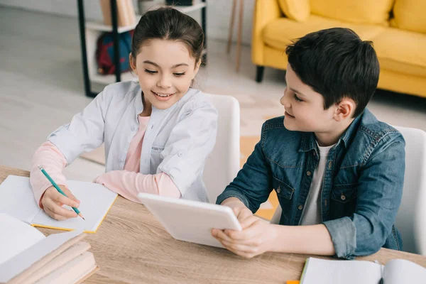 Entzückender Bruder und Schwester sitzen am Tisch und machen zu Hause gemeinsam Hausaufgaben — Stockfoto