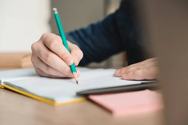 Selektiver Fokus des Schülers, der in Notizbuch schreibt, während er Hausaufgaben macht — Stockfoto
