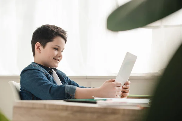 Enfoque selectivo del niño sonriente usando tableta digital mientras hace el trabajo escolar en casa - foto de stock