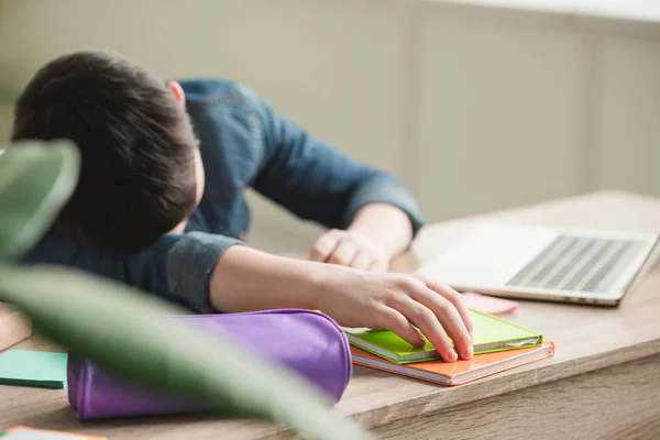 Selective focus of tired boy sleeping at table near copy books and laptop — Stock Photo