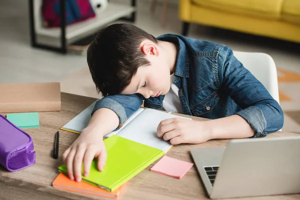 Adorable exhausted boy sleeping at table near copy books and laptop — Stock Photo