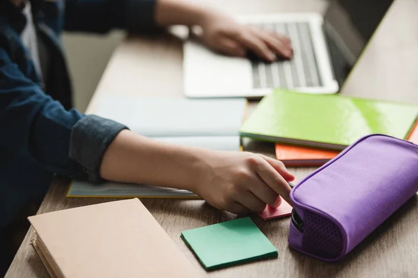 Vista ritagliata di scolaro utilizzando il computer portatile mentre seduto alla scrivania con libri di copia e fare i compiti — Foto stock