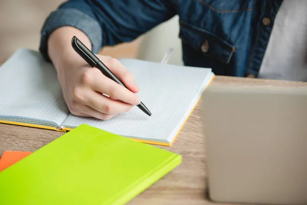 Vista ritagliata dello scolaro che scrive nel notebook mentre fa i compiti a casa — Foto stock