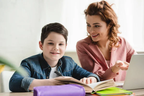 Fröhliche Mutter mit entzückendem Sohn bei gemeinsamen Schularbeiten zu Hause — Stockfoto