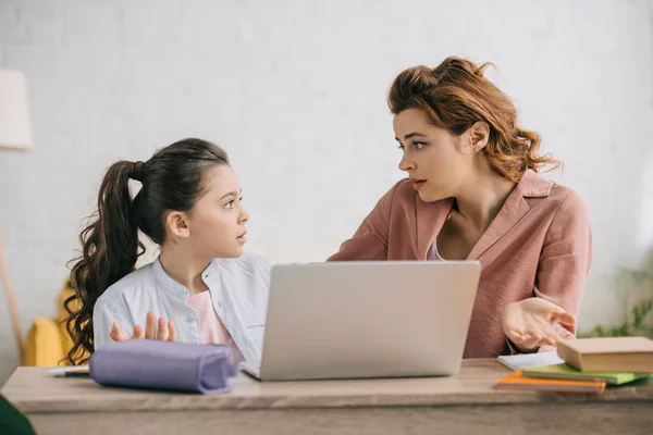 Mujer desalentada mostrando gesto de encogimiento mientras usa el ordenador portátil junto con su hija - foto de stock