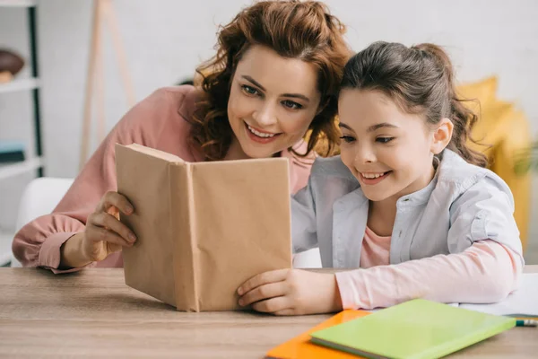 Heureux mère et fille assis à la table en bois et le livre de lecture ensemble — Photo de stock