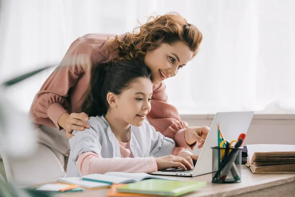 Feliz madre ayudando sonriente hija haciendo trabajo escolar en casa - foto de stock