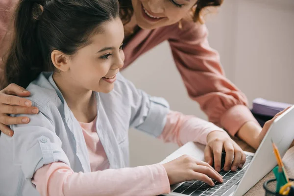 Selective focus of smiling child using laptop near smiling mother — Stock Photo