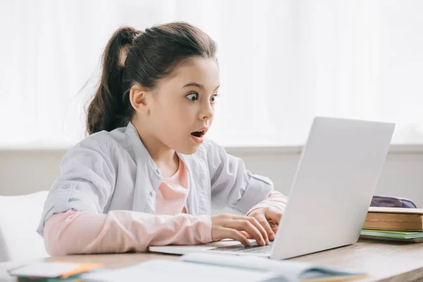 Überraschtes Kind benutzt Laptop während es am Schreibtisch sitzt und zu Hause Hausaufgaben macht — Stockfoto