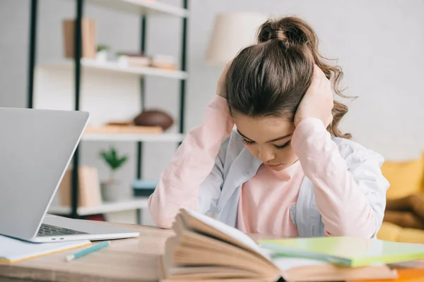 Müdes Schulkind, das die Hände auf dem Kopf hält, während es am Schreibtisch sitzt und zu Hause Hausaufgaben macht — Stockfoto