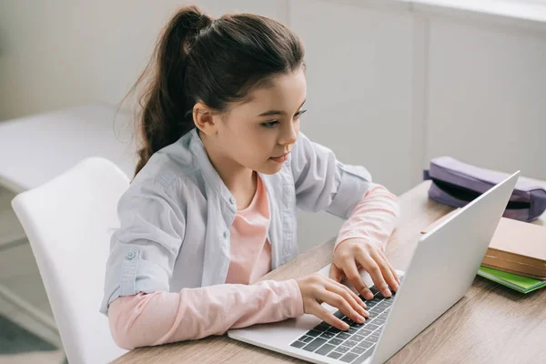 Aufmerksames Schulkind benutzt Laptop während es am Schreibtisch sitzt und Hausaufgaben macht — Stockfoto