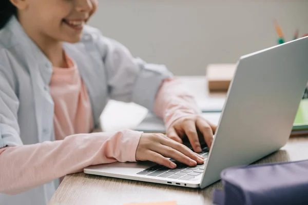 Visão parcial de estudante sorrindo usando laptop enquanto faz trabalhos escolares em casa — Fotografia de Stock