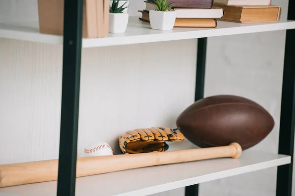 Rack com luva de beisebol e bola, bola de rugby, livros e vasos de flores — Fotografia de Stock