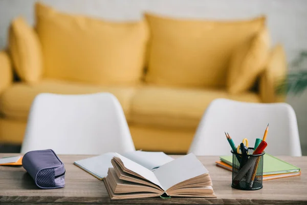 Foco selectivo de escritorio de madera con libro abierto, libros de copia, estuche de lápiz y papelería - foto de stock