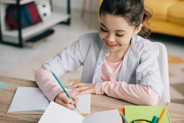 Vista ad alto angolo di adorabile bambino che fa i compiti e scrive nel quaderno — Foto stock