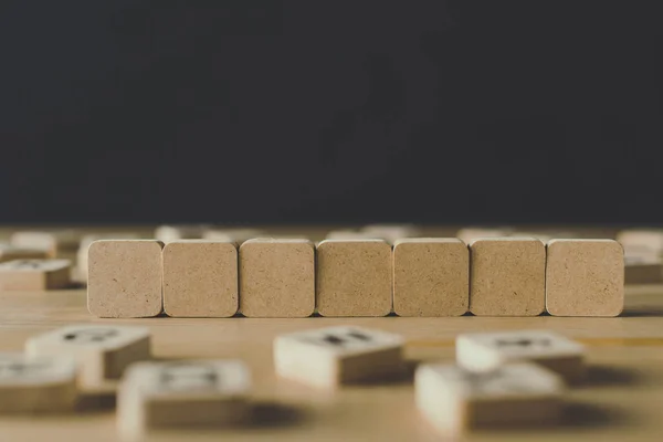 Selektive Fokussierung von sieben leeren Würfeln, umgeben von Blöcken mit Buchstaben auf hölzerner Oberfläche, isoliert auf schwarz — Stockfoto