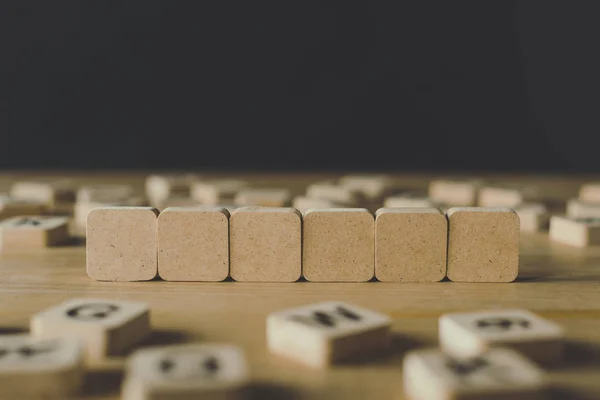 Selektive Fokussierung von sechs leeren Würfeln, umgeben von Blöcken mit Buchstaben auf hölzerner Oberfläche, isoliert auf schwarz — Stockfoto