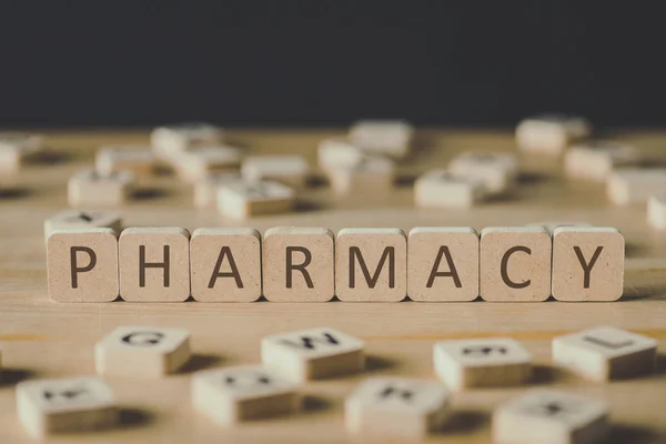 Enfoque selectivo de la inscripción de farmacia en cubos rodeados de bloques con letras en la superficie de madera aislada en negro - foto de stock