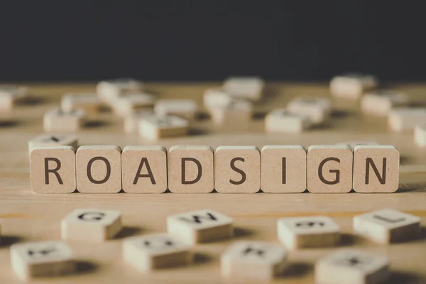 Selective focus of word roadsign made of cubes surrounded by blocks with letters on wooden surface isolated on black — Stock Photo