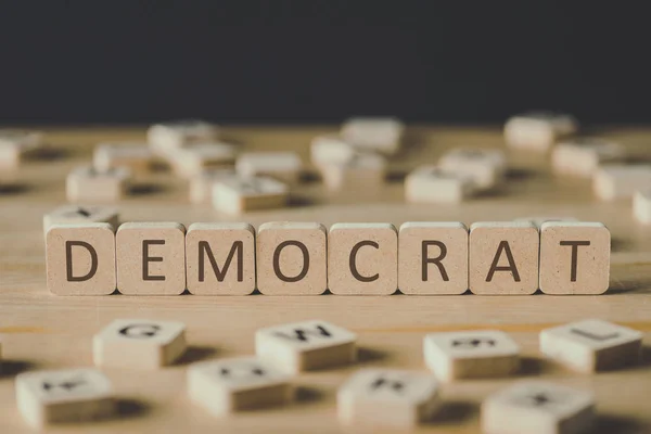 Selective focus of word democrat made of cubes surrounded by blocks with letters on wooden surface isolated on black — Stock Photo