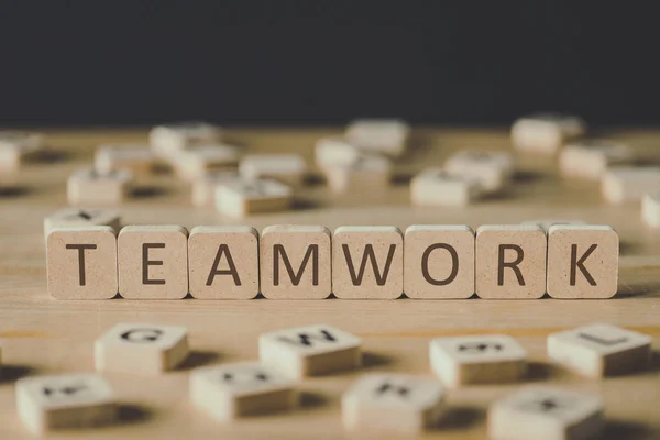 Selective focus of word teamwork made of cubes surrounded by blocks with letters on wooden surface isolated on black — Stock Photo