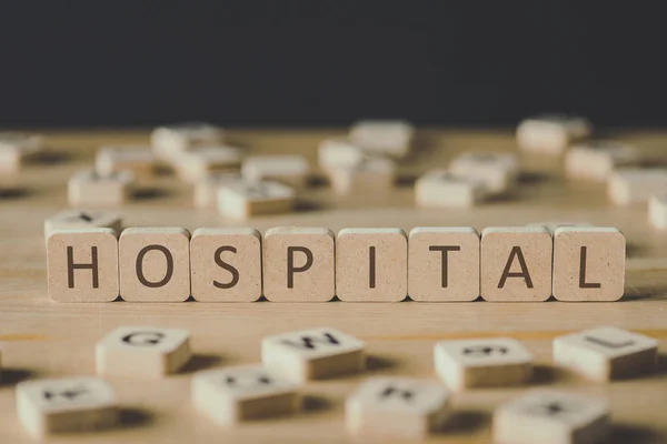 Selective focus of cubes with word hospital surrounded by blocks with letters on wooden surface isolated on black — Stock Photo
