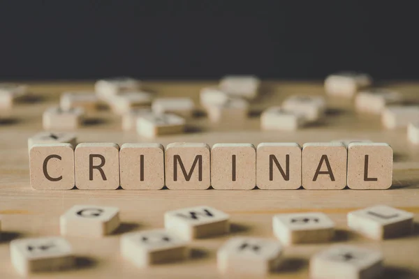 Selective focus of criminal lettering on cubes surrounded by blocks with letters on wooden surface isolated on black — Stock Photo
