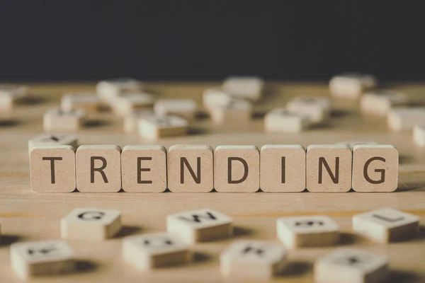 Selective focus of word trending made of cubes surrounded by blocks with letters on wooden surface isolated on black — Stock Photo